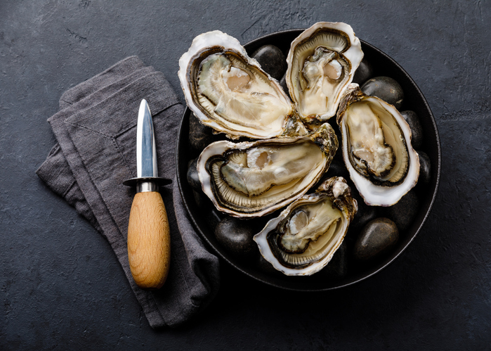 Fresh Oysters with lemon and knife on stones on dark backgroundOysters and knife